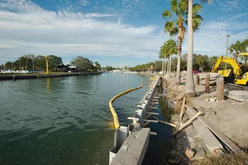 Tuinposter Horizontal shot Seawall repair in Gulfport, Florida east side of marina. Late afternoon sun with water on left and dirt, metal and concrete beam. Wood pilings on the right and yellow boom in water. © Del Harper