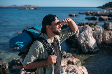 Obraz premium A male tourist with a large backpack and hiking gear on a rocky seashore.