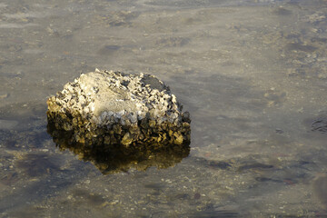 One tan bright rock in middle left corner on a sunny day. Above the calm blue water with small...