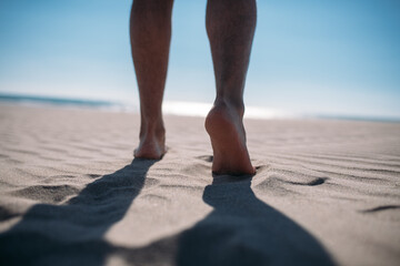 Men's bare feet on the sand. Close-up of the legs.