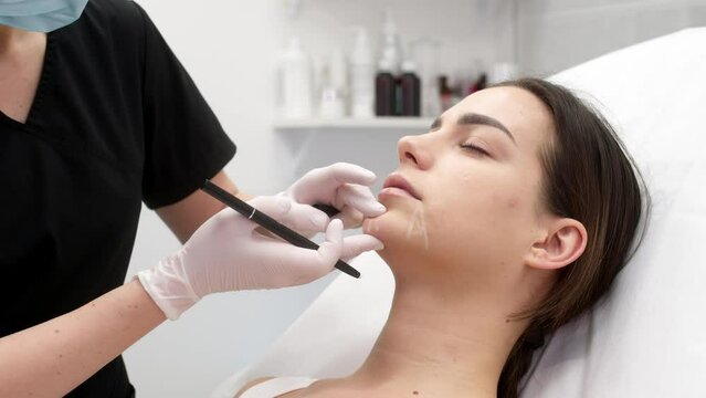 The cosmetologist marks with a pen for the injection on patient&rsquo;s forehead. Concept of preparation for beauty injection. Youthfulness, comfort, facial care