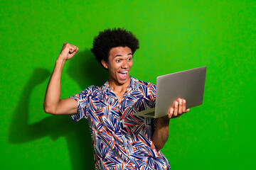 Photo of lucky impressed guy wear print shirt rising fist getting likes modern device isolated...