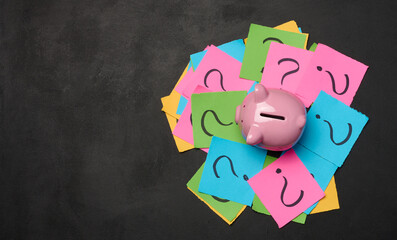  Ceramic piggy bank and stickers with drawn question marks on a black background, top view
