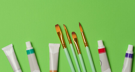 Tubes with oil paint and brushes on a green background, top view