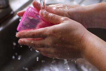 manos de mujer lavando vaso de color rosa.