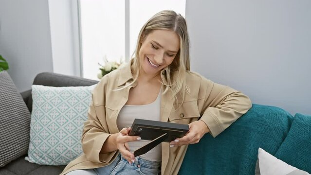 Young blonde woman sitting on sofa holding picture smiling at home
