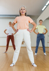Obraz premium Portrait of cheerful active female pensioner exercising dance moves in fitness studio