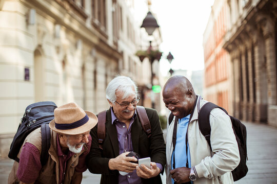 Group of male senior friends exploring a city and using a phone on their vacation