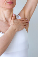 Shot of the woman in the white top against the white wall, performing self examination of the breasts, looking for abnormalities. Cancer awareness