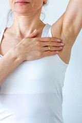 Shot of the woman in the white top against the white wall, performing self examination of the breasts, looking for abnormalities. Cancer awareness