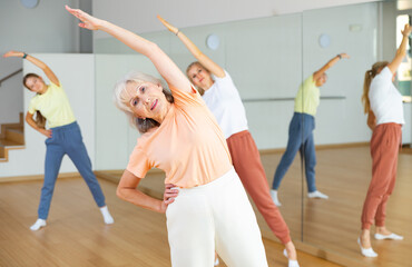 Positive mature woman doing aerobics exercises with group of people in dance center