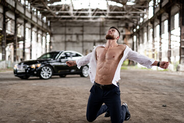 Young man is kneeling on the floor in abandoned building with his arms outstretched.