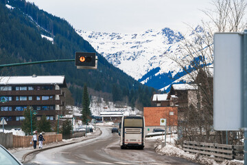 A serene winter scene captures a town nestled against snow-capped mountains, an amber traffic light glowing amidst the chilly air. Ideal for concepts of travel, seasons, or nature majesty