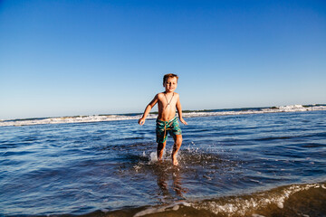 Fototapeta premium Kid bathing in the sea. Boy having fun in the ocean waves at sunset on a sunny summer vacation day. Child having fun outdoors.