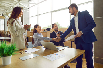 Business people shaking hands celebrating success, making a deal, business achievement or signing a contract on their workplace. Group of company employees in office applauding to their coworkers.