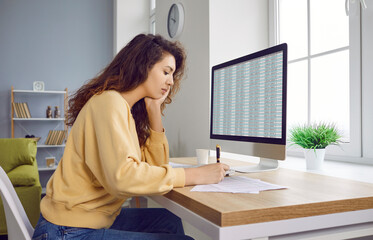 Young woman financial accountant working from home, sitting at desk with computer, using digital...