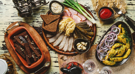 Set appetizer for vodka, boiled potatoes with herring fish, meat platter with ham, bacon, lard, pickles and fried slices of dry bread on rustic background. Homemade food, top view, toning