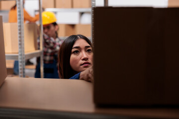 Asian woman warehouse worker doing inventory management while checking customer parcels on shelf. Logistics manager searching cardboard box in distribution center storehouse - obrazy, fototapety, plakaty