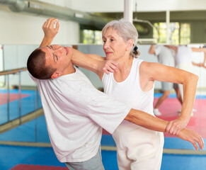 Fototapeta na wymiar Elderly woman is training with man on the self-defense course in gym