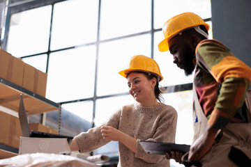 Diverse coworkers wearing industrail overall and helmet, while checking online orders on laptop...