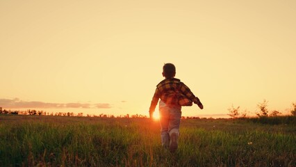Dream kid Joyful little boy running at sunset. Child boy runs through green grass in sun. Childhood dream happiness concept. Happy child playing in nature. Kid is running across field. Happy family.