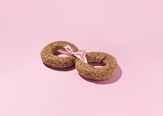 Two bagels sprinkled with sesame seeds, tied with a pink satin bow, a romantic couple