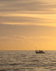 A boat sailing on the sea with clouds and the horizon in the background. Silhouette of a fishing boat sailing alone in the vastness of the sea at sunrise.