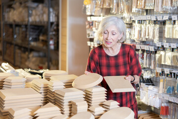 Elderly woman in casual clothes chooses blanks for pottery in shop
