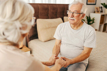A romantic senior couple is holding hands in bedroom.