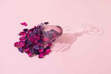 Pink and purple decorative leaves spilled from a drinking glass . Pastel pink background. Minimal holiday drink aesthetic concept.