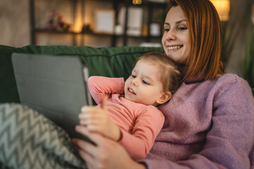 Mother and daughter use digital tablet to watch online video at home