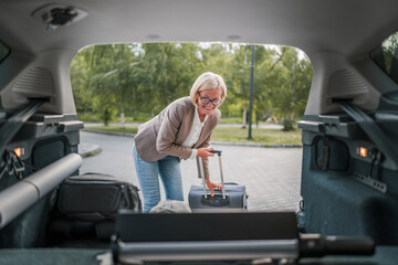 Obraz premium mature blonde woman travel take stuff belongings from the back of car