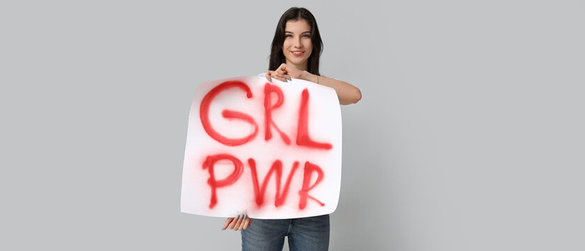 Young woman holding placard with slogan GRL PWR on light background. Feminism concept