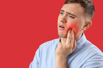 Young man having toothache on red background