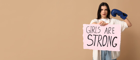Young woman holding paper with slogan GIRLS ARE STRONG on beige background with space for text....