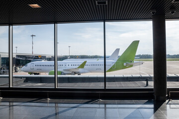 View of a commercial passenger airplane from an airport terminal window, showcasing the aircraft awaiting departure on the tarmac, ready for taxiing and takeoff.