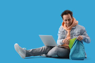 Male student with laptop and backpack on blue background