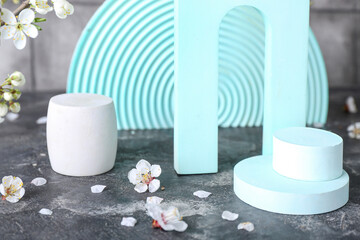 Podiums with blooming branches on table near grey tile wall, closeup. Hello spring