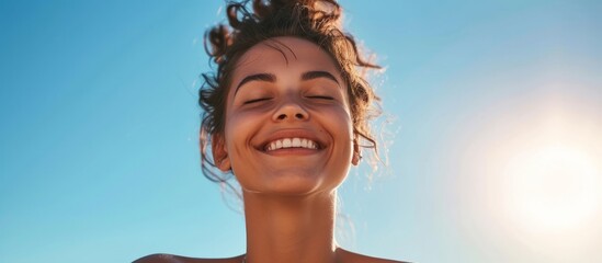 Fit young woman smiles while deep breathing in front of a clear blue sky on a sunny and windy summer day. - obrazy, fototapety, plakaty