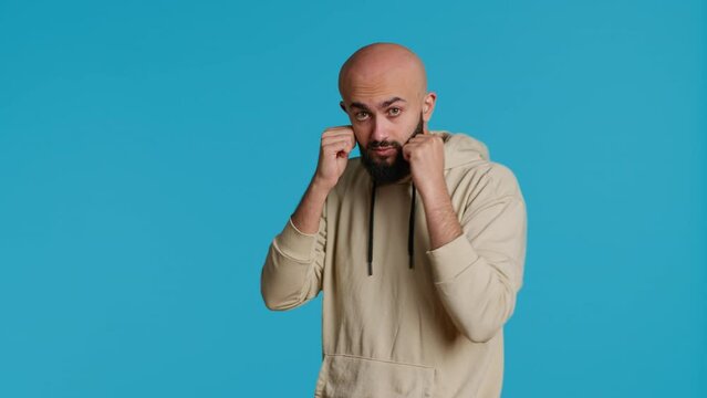 Muslim male model acting aggressive with clenched fists, preparing to fight and punch someone on camera. Arab person being violent and boxing in studio, strong man with fighter pose. Camera 1.