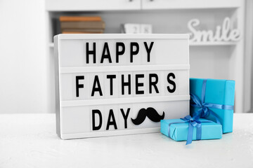 Board with text HAPPY FATHER'S DAY and gifts on table in room