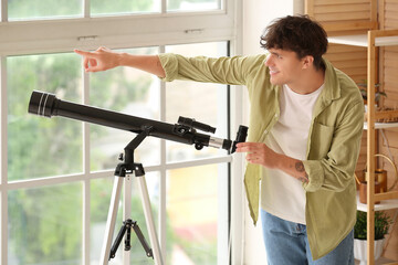 Young man with telescope near window at home