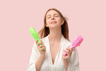 Beautiful young woman with handheld mini fans on pink background