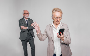 Senior female executive using smartphone and showing stop gesture to businessman on white background