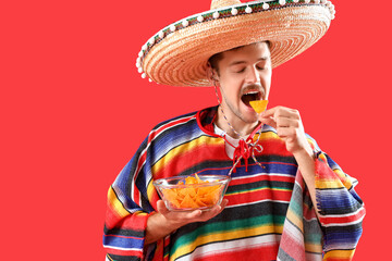 Young Mexican man eating nachos on red background