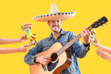 Young man playing guitar and hands with Mexican symbols on yellow background