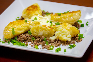 Traditional Ukrainian pierogi grilled in butter and served with minced meat and cream, decorated with fresh fine herbs