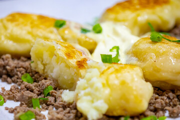 Traditional Ukrainian pierogi grilled in butter and served with minced meat and cream, decorated with fresh fine herbs