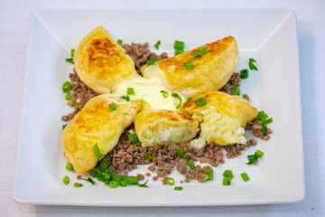 Traditional Ukrainian pierogi grilled in butter and served with minced meat and cream, decorated with fresh fine herbs