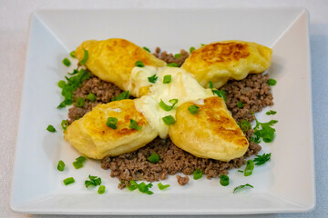 Traditional Ukrainian pierogi grilled in butter and served with minced meat and cream, decorated with fresh fine herbs